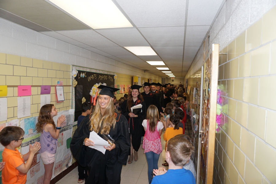 graduates walking past small children