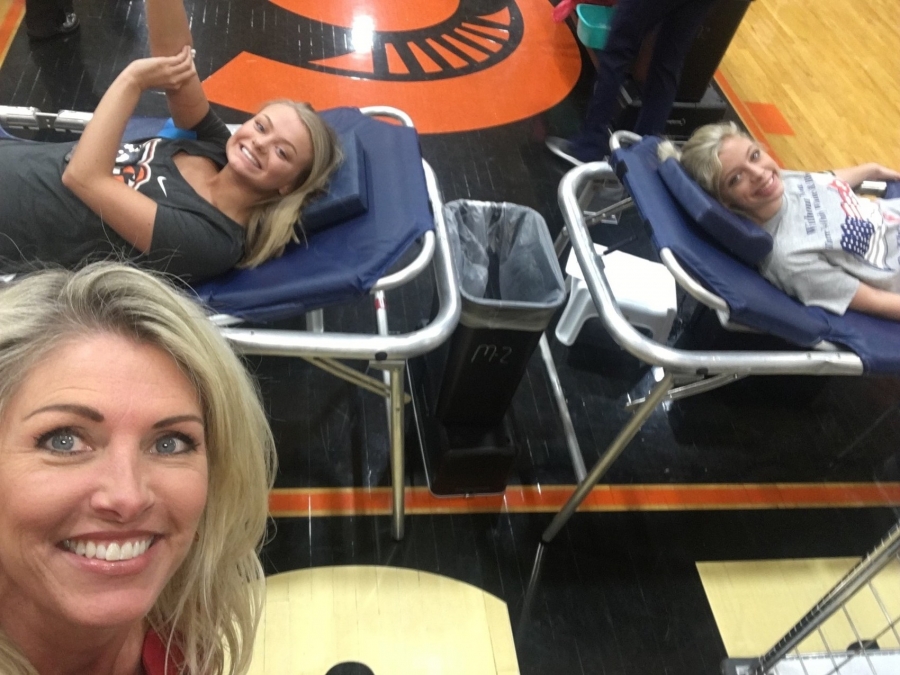 two girls laying on a table giving blood with a selfie face in the front